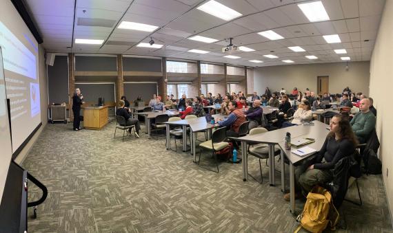 Attendees sit at tables and look forward as Heidi McKee delivers her talk.