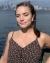 C. R. squinting with a closed lip smile at the sun, hair back in two french braids, wearing a floral spaghetti strap tank top and resin pink and brown dangle earrings. The Seattle skyline is blurred in the background.