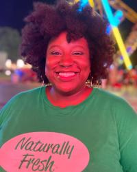 Photo of a Black woman with an afro smiling under neon lights