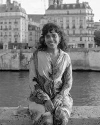 Image of woman sitting in front of river with Paris behind her
