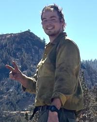 Smiling, making peace sign, standing on a mountain ridge in work clothes