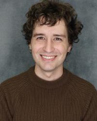 Picture of brown-haired, brown-eyed 29-year-old Alex Henry. They're smiling and have a cute sweater on.