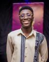 The image shows me smiling warmly at the camera. I am wearing glasses and a beige long-sleeve shirt that features a striking design with black and white traditional patterns running vertically down the front and along one shoulder.