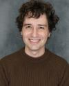 Picture of brown-haired, brown-eyed 29-year-old Alex Henry. They're smiling and have a cute sweater on.