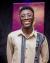 The image shows me smiling warmly at the camera. I am wearing glasses and a beige long-sleeve shirt that features a striking design with black and white traditional patterns running vertically down the front and along one shoulder.
