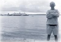 A blue-tinted picture of John Webster, posing in front of a ferry.