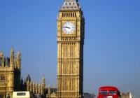 Big Ben, London, with two red double-decker buses driving by.