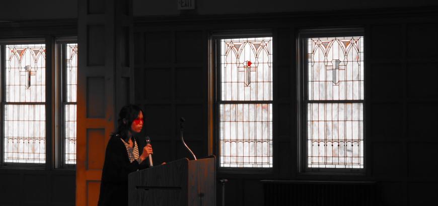 MFA student in sunglasses reads at a podium