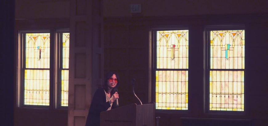 MFA student in sunglasses reads at a podium